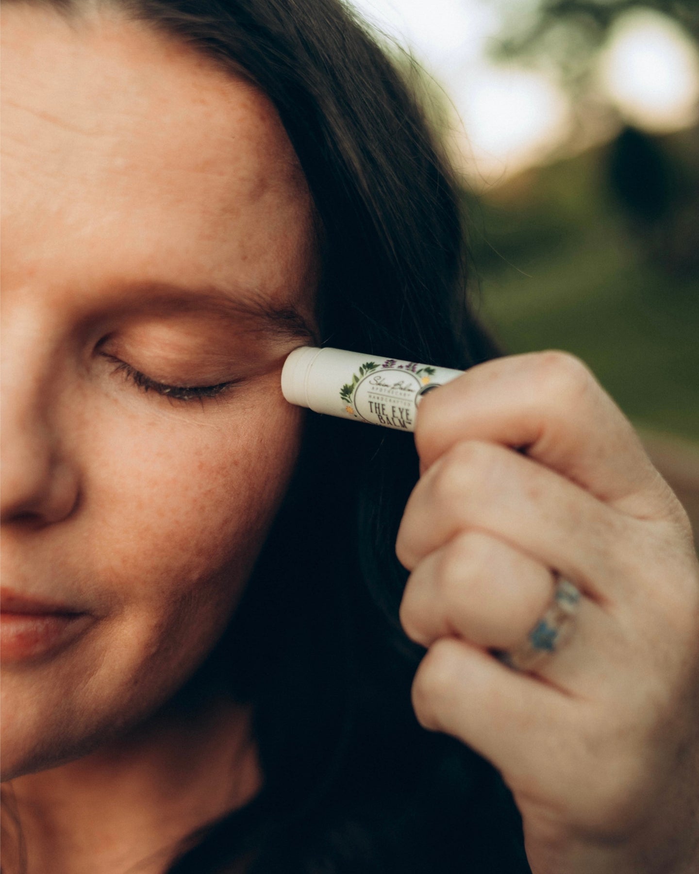 A close-up shot of a woman with her eyes closed applying The Eye Balm™.